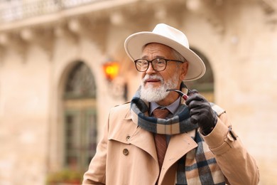 Stylish senior man with tobacco pipe on city street