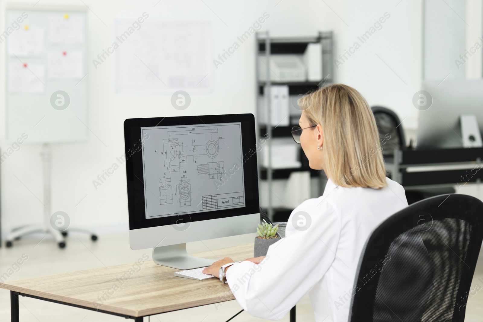 Photo of Technician making digital engineering drawing on computer at desk in office, back view