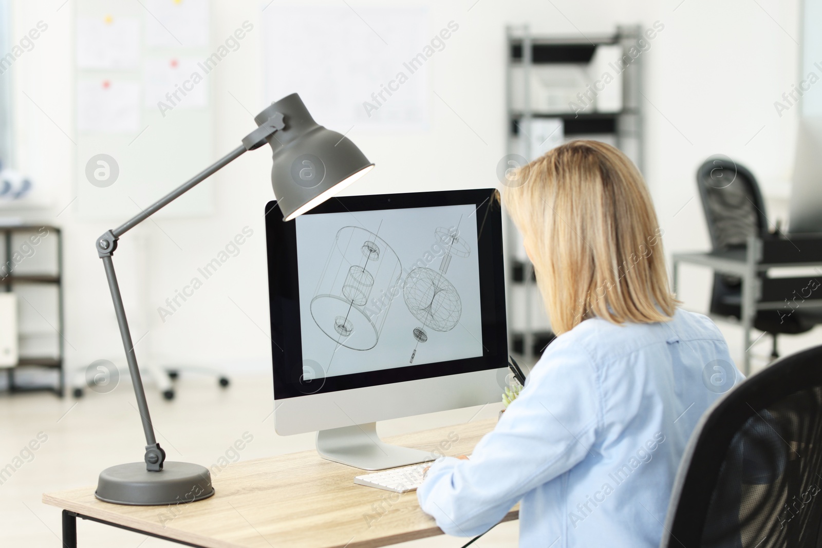 Photo of Technician making digital engineering drawing on computer at desk in office, back view