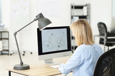 Photo of Technician making digital engineering drawing on computer at desk in office, back view