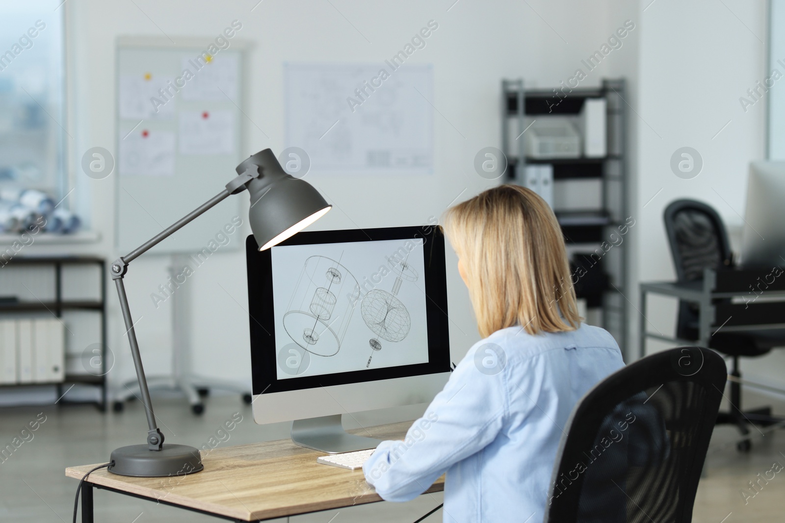 Photo of Technician making digital engineering drawing on computer at desk in office, back view