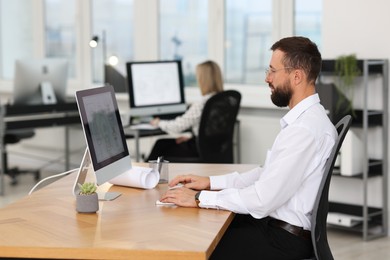 Technician making digital engineering drawing on computer at desk in office