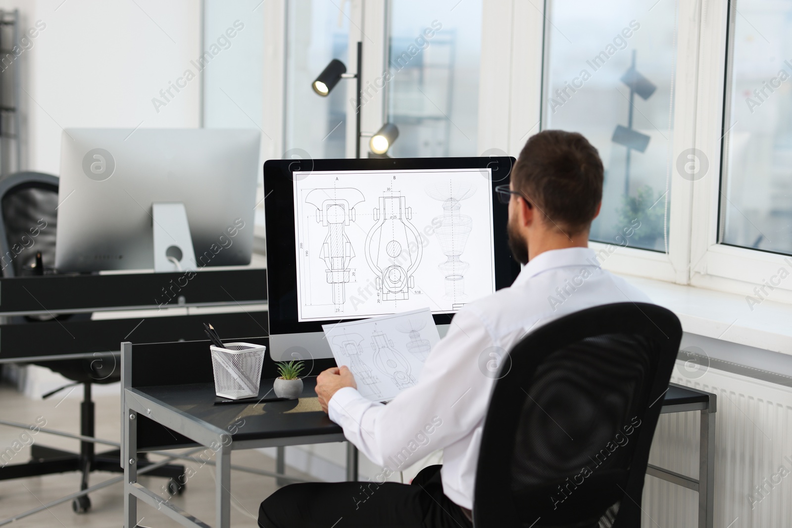 Photo of Technician making digital engineering drawing on computer at desk in office, back view