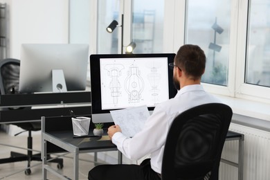 Photo of Technician making digital engineering drawing on computer at desk in office, back view