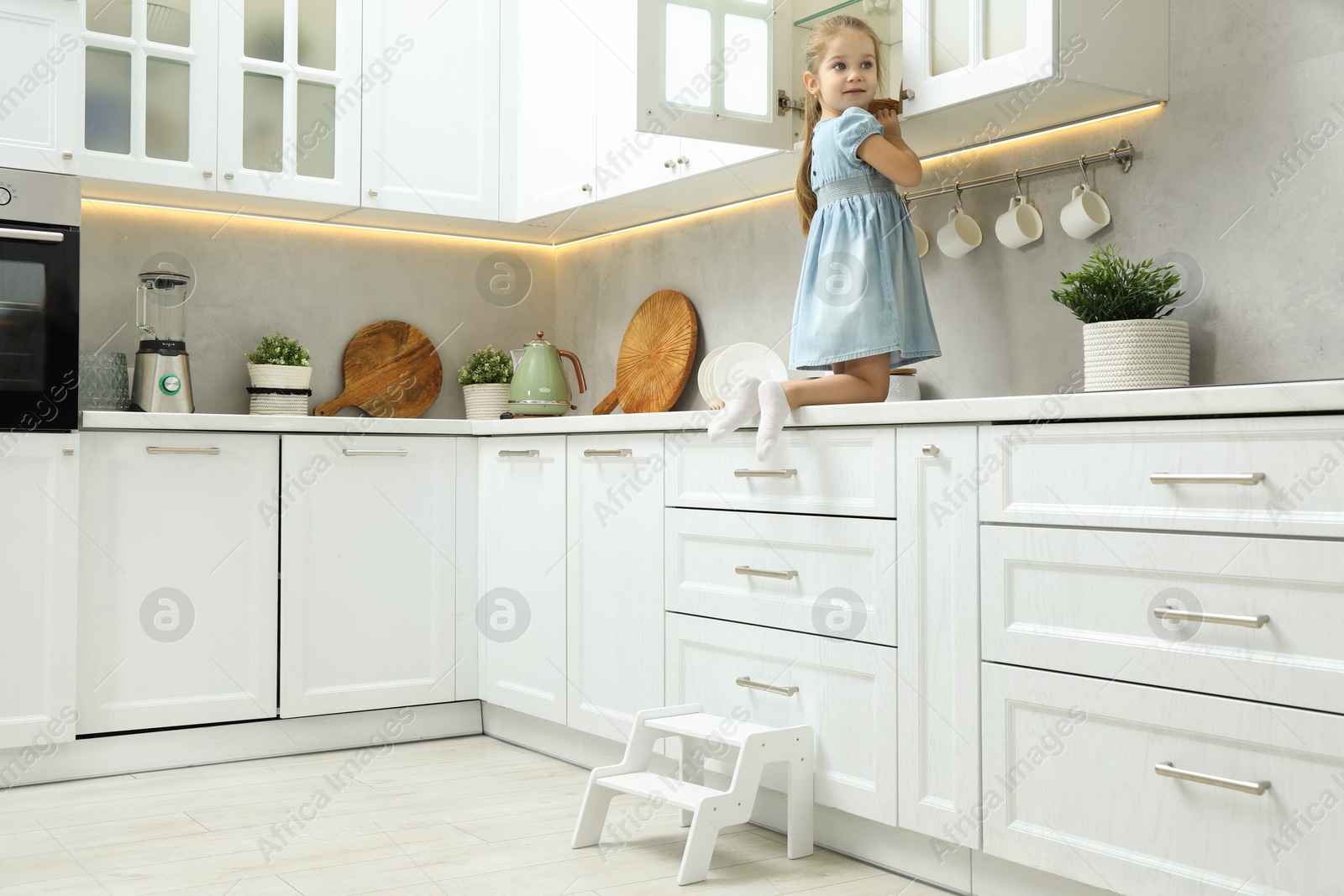 Photo of Little girl sitting on counter near step stool in kitchen