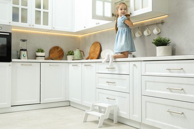 Little girl sitting on counter near step stool in kitchen