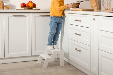 Photo of Little boy standing on step stool near countertop in kitchen