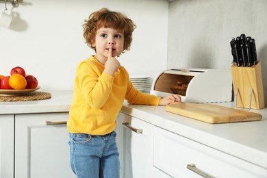 Photo of Little boy showing shush gesture near countertop in kitchen