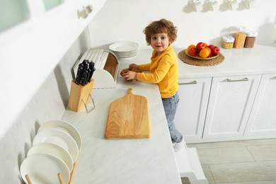 Little boy standing on step stool near countertop with cookies in kitchen