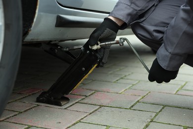 Photo of Auto mechanic lifting car with scissor jack outdoors, closeup