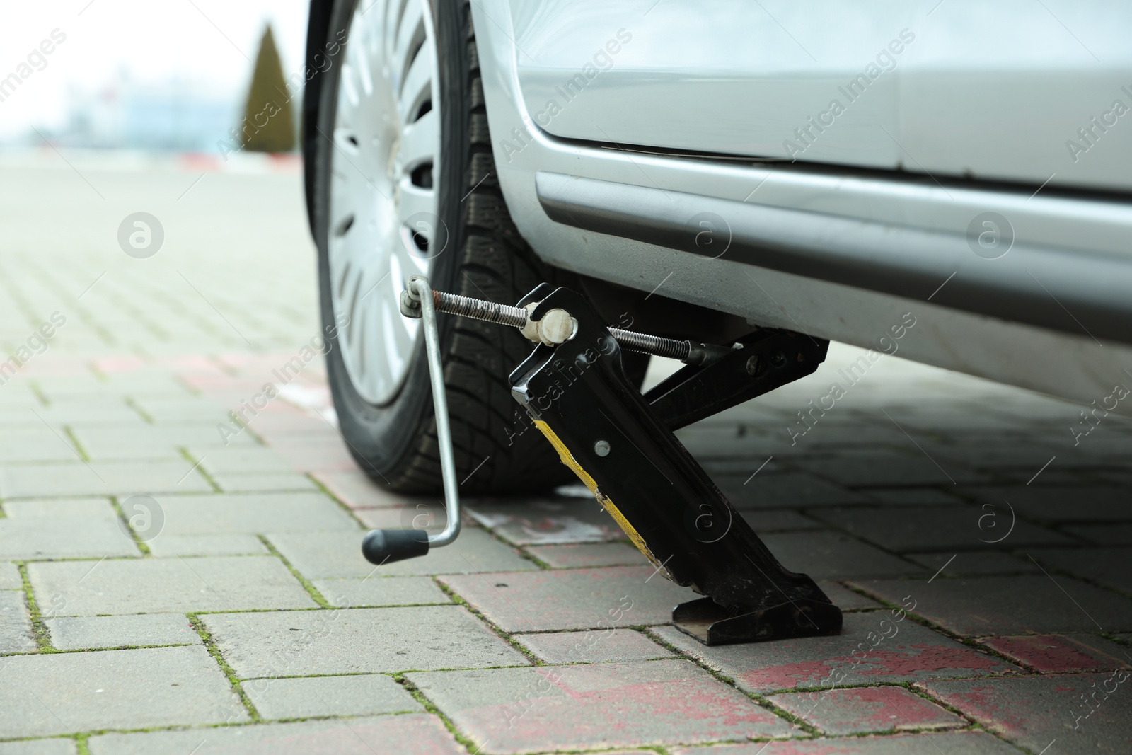 Photo of Car lifted by scissor jack on roadside outdoors