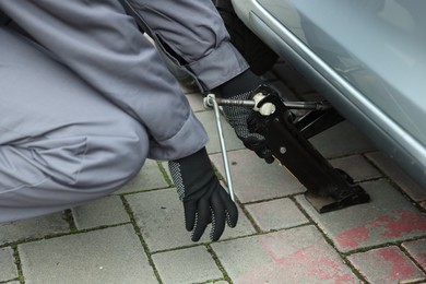 Photo of Auto mechanic lifting car with scissor jack outdoors, closeup