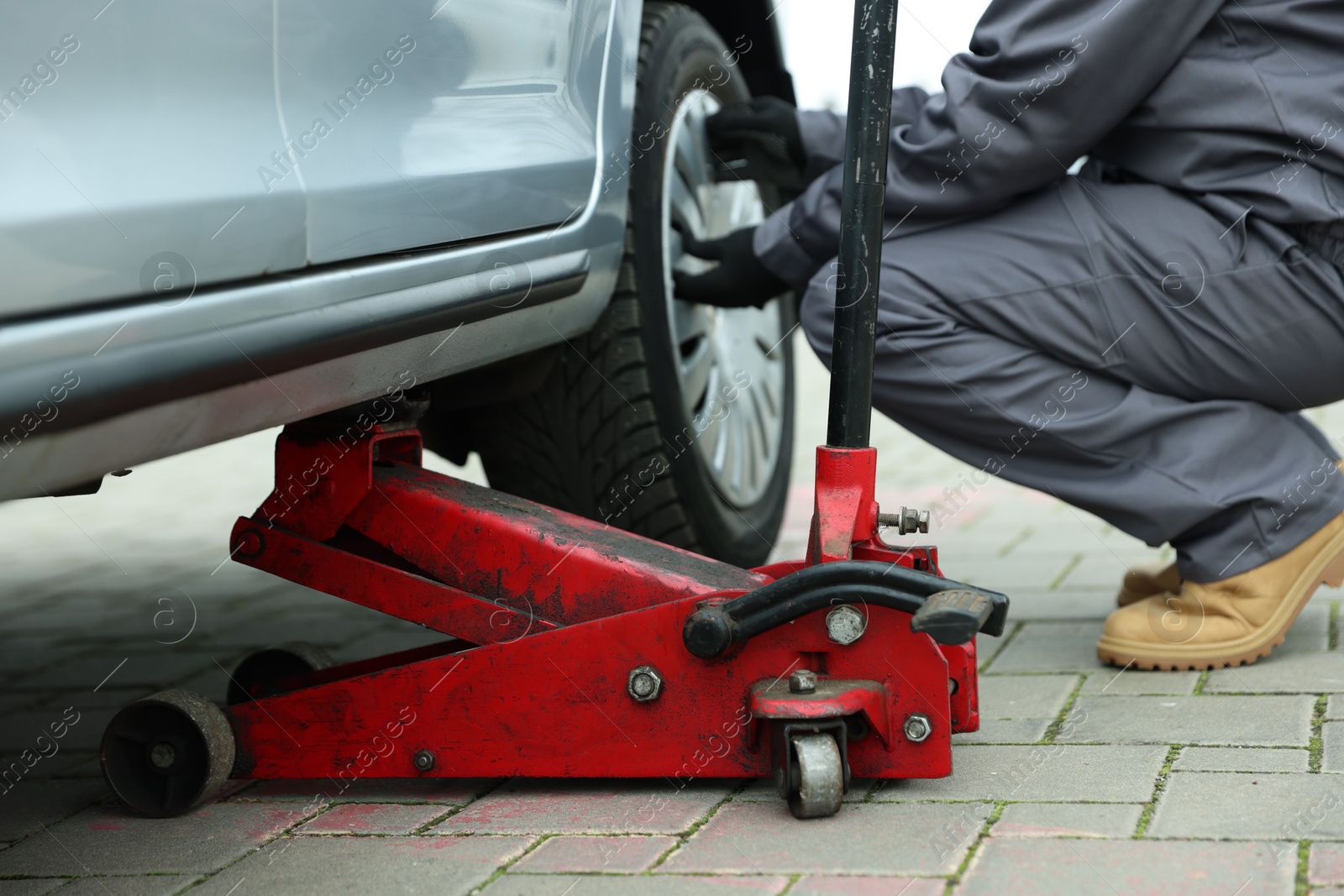 Photo of Car lifted by scissor jack. Auto mechanic changing wheel outdoors, closeup