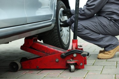 Photo of Car lifted by scissor jack. Auto mechanic changing wheel outdoors, closeup