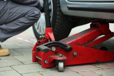 Photo of Car lifted by scissor jack. Auto mechanic changing wheel outdoors, closeup