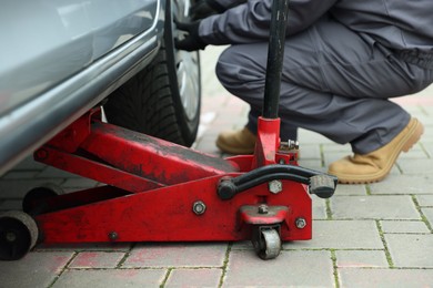 Photo of Car lifted by scissor jack. Auto mechanic changing wheel outdoors, closeup