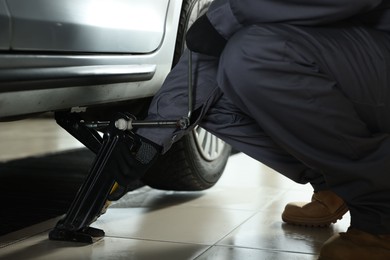 Photo of Auto mechanic lifting car with scissor jack at service station, closeup