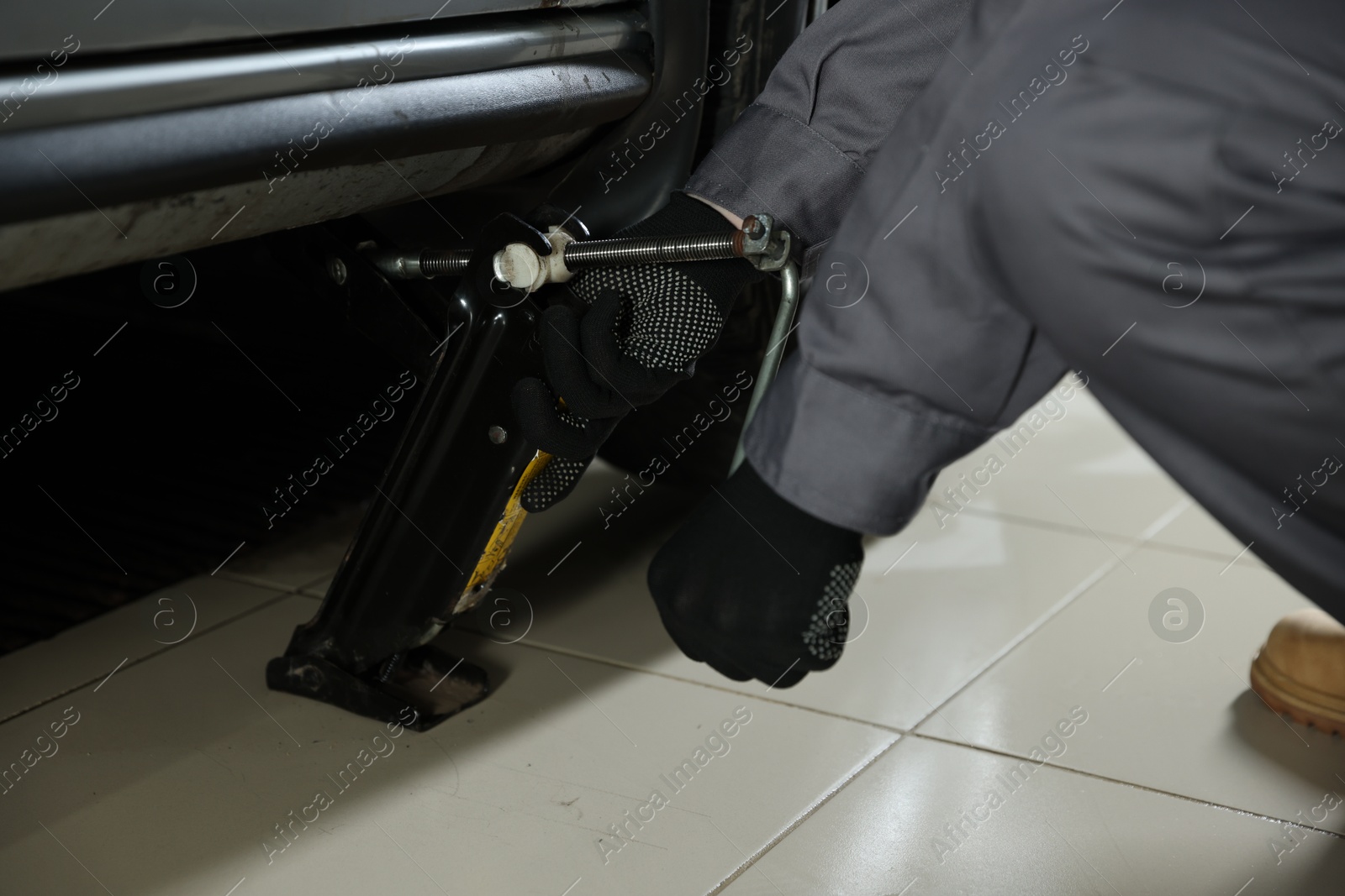 Photo of Auto mechanic lifting car with scissor jack at service station, closeup