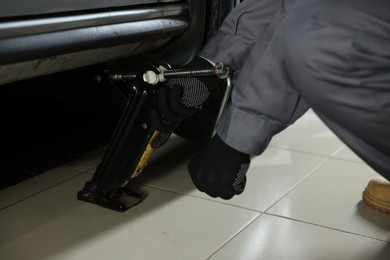 Photo of Auto mechanic lifting car with scissor jack at service station, closeup