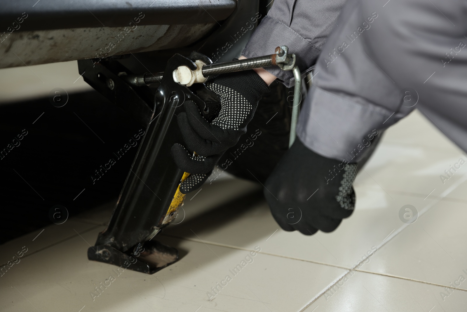 Photo of Auto mechanic lifting car with scissor jack at service station, closeup