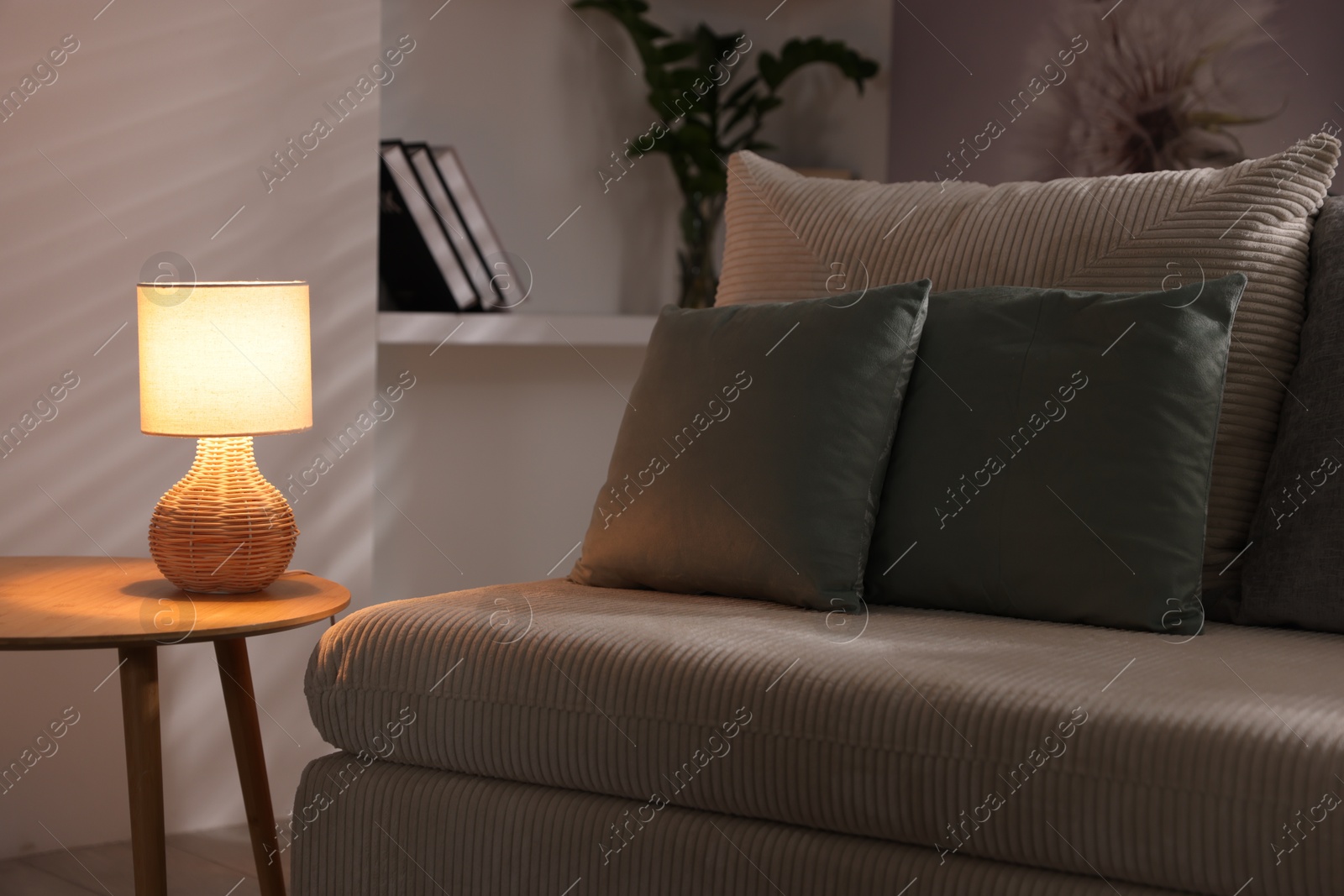 Photo of Stylish night lamp on wooden table and sofa in room. Interior design