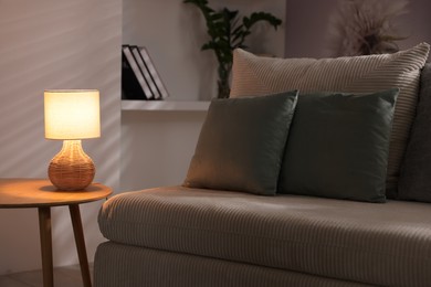 Photo of Stylish night lamp on wooden table and sofa in room. Interior design