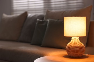 Photo of Stylish night lamp on wooden table and sofa in room, space for text