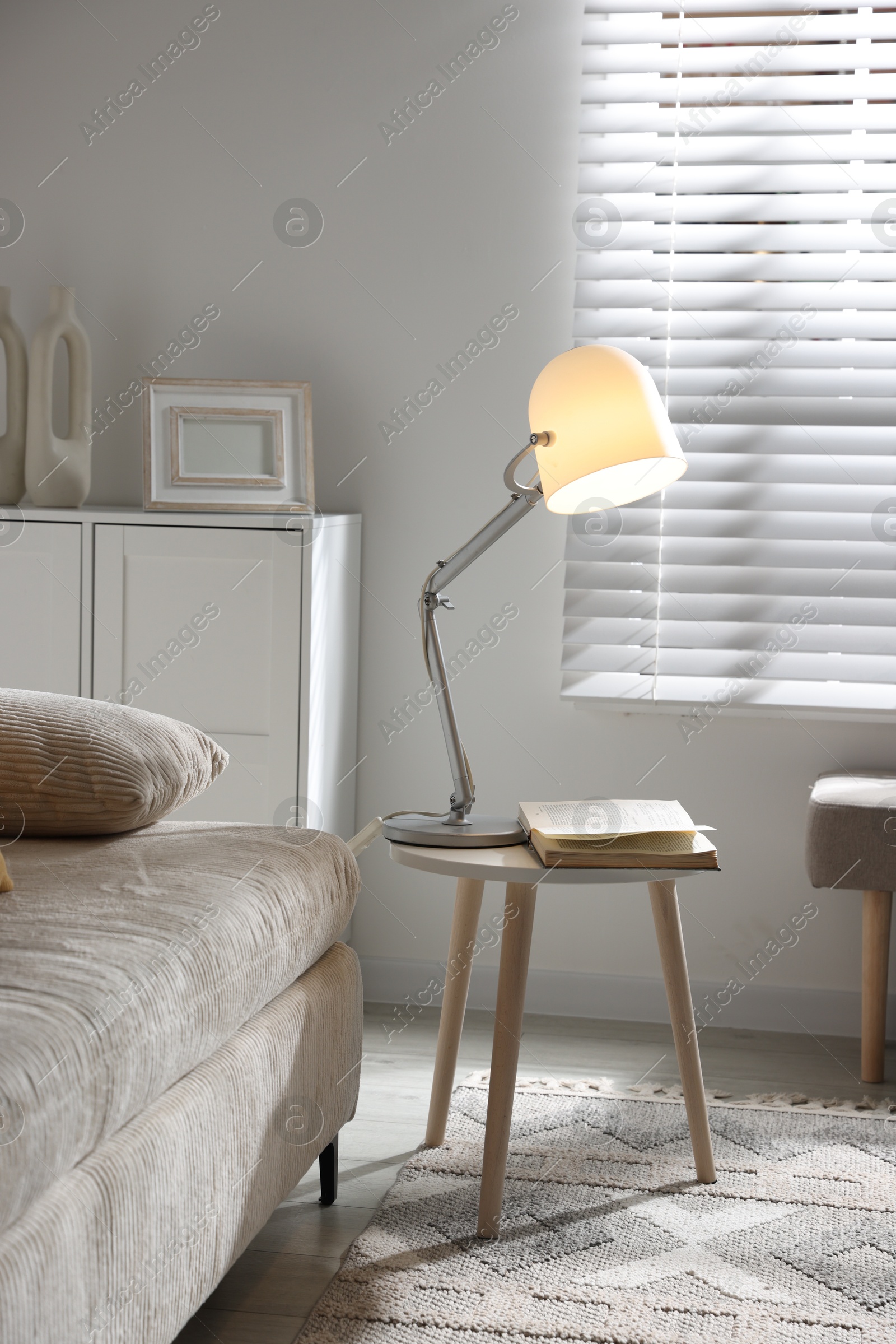 Photo of Stylish night lamp and book on side table near sofa in room. Interior design