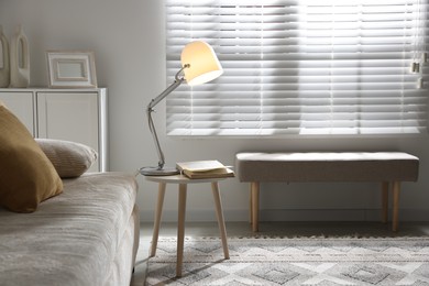 Photo of Stylish night lamp and book on side table near sofa in room. Interior design