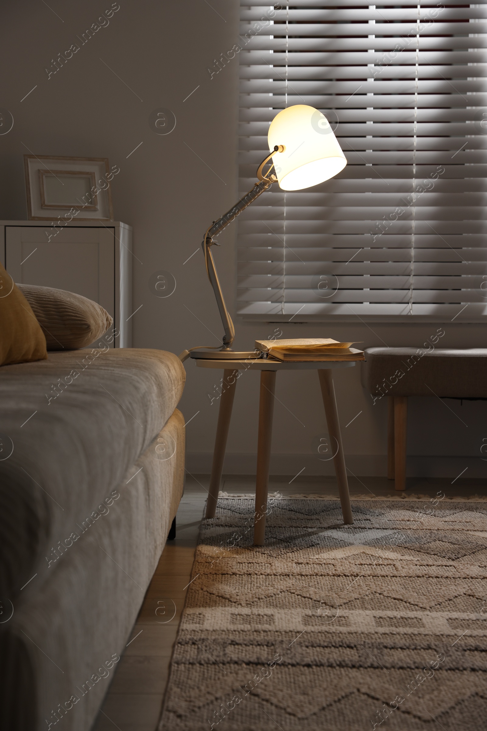 Photo of Stylish night lamp and book on side table near sofa in room. Interior design