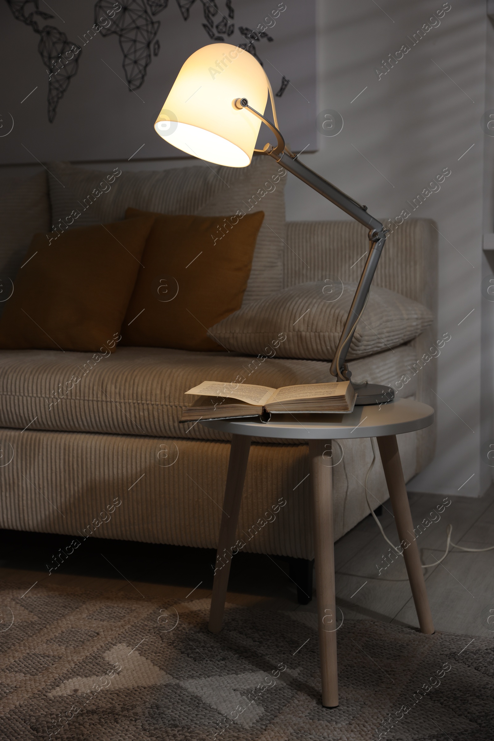 Photo of Stylish night lamp and book on side table near sofa in room. Interior design