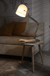 Photo of Stylish night lamp and book on side table near sofa in room. Interior design