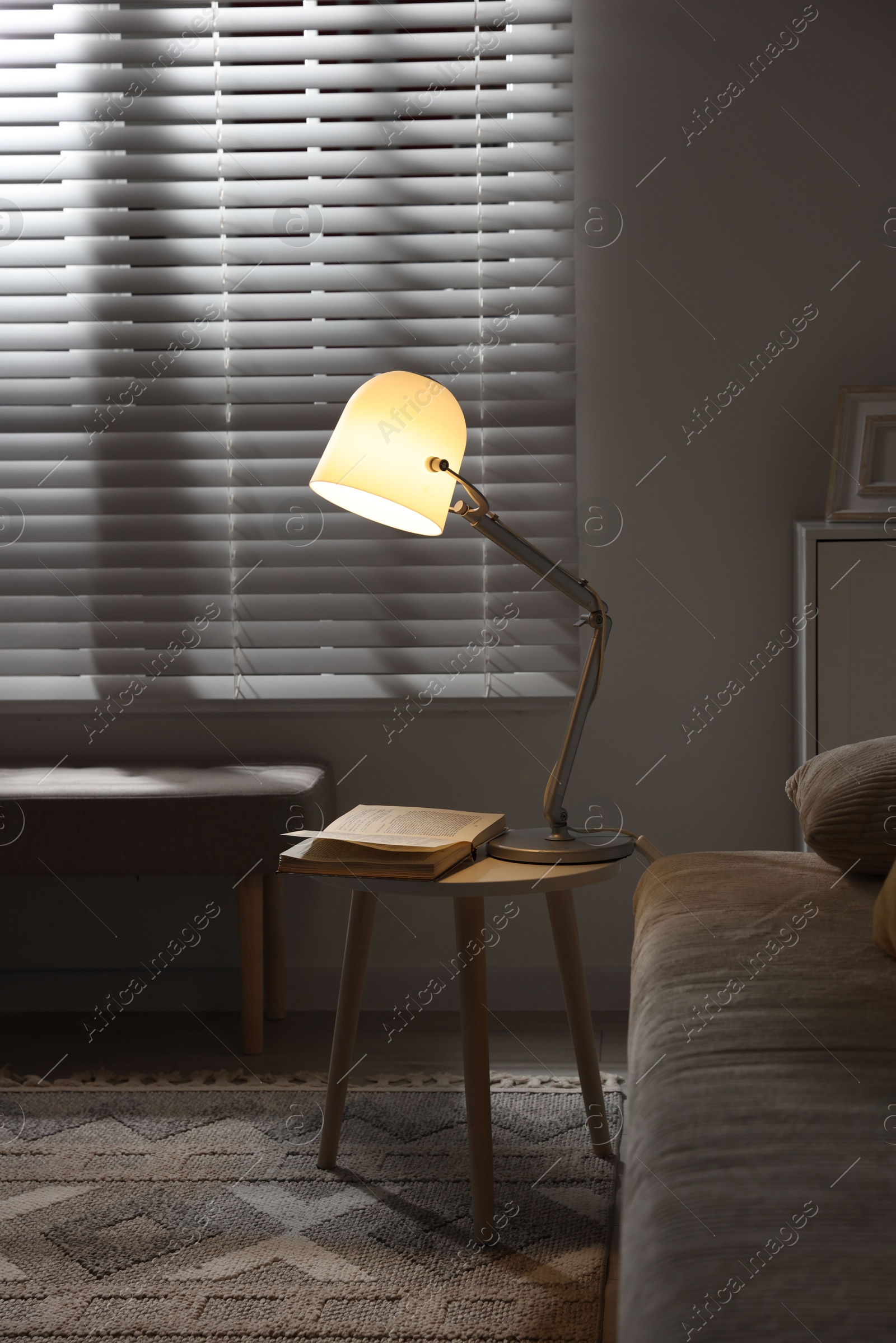 Photo of Stylish night lamp and book on side table near sofa in room. Interior design