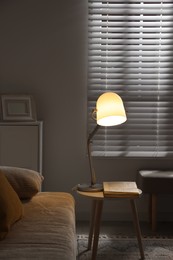 Photo of Stylish night lamp and book on side table near sofa in room. Interior design