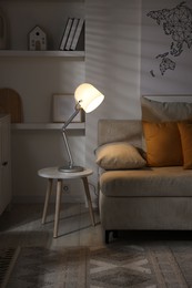 Photo of Stylish night lamp on side table near sofa in room. Interior design