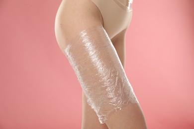 Photo of Woman doing spa body wraps on her leg against pink background, closeup