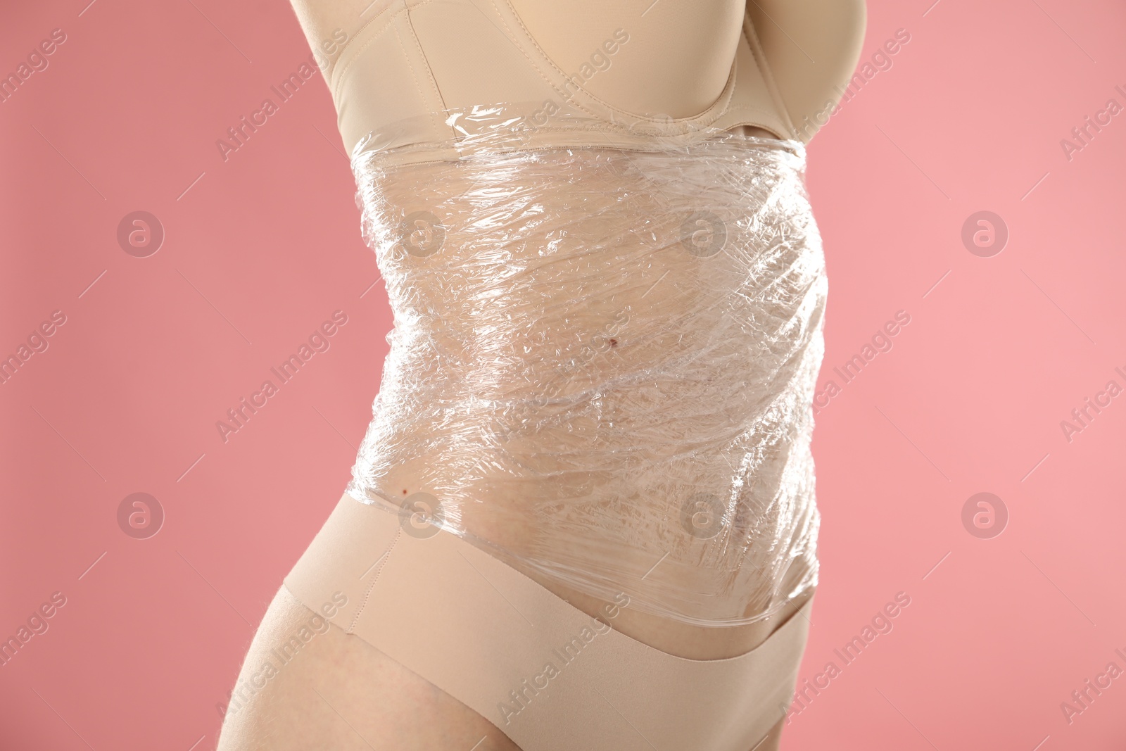 Photo of Woman doing spa body wraps on her belly against pink background, closeup