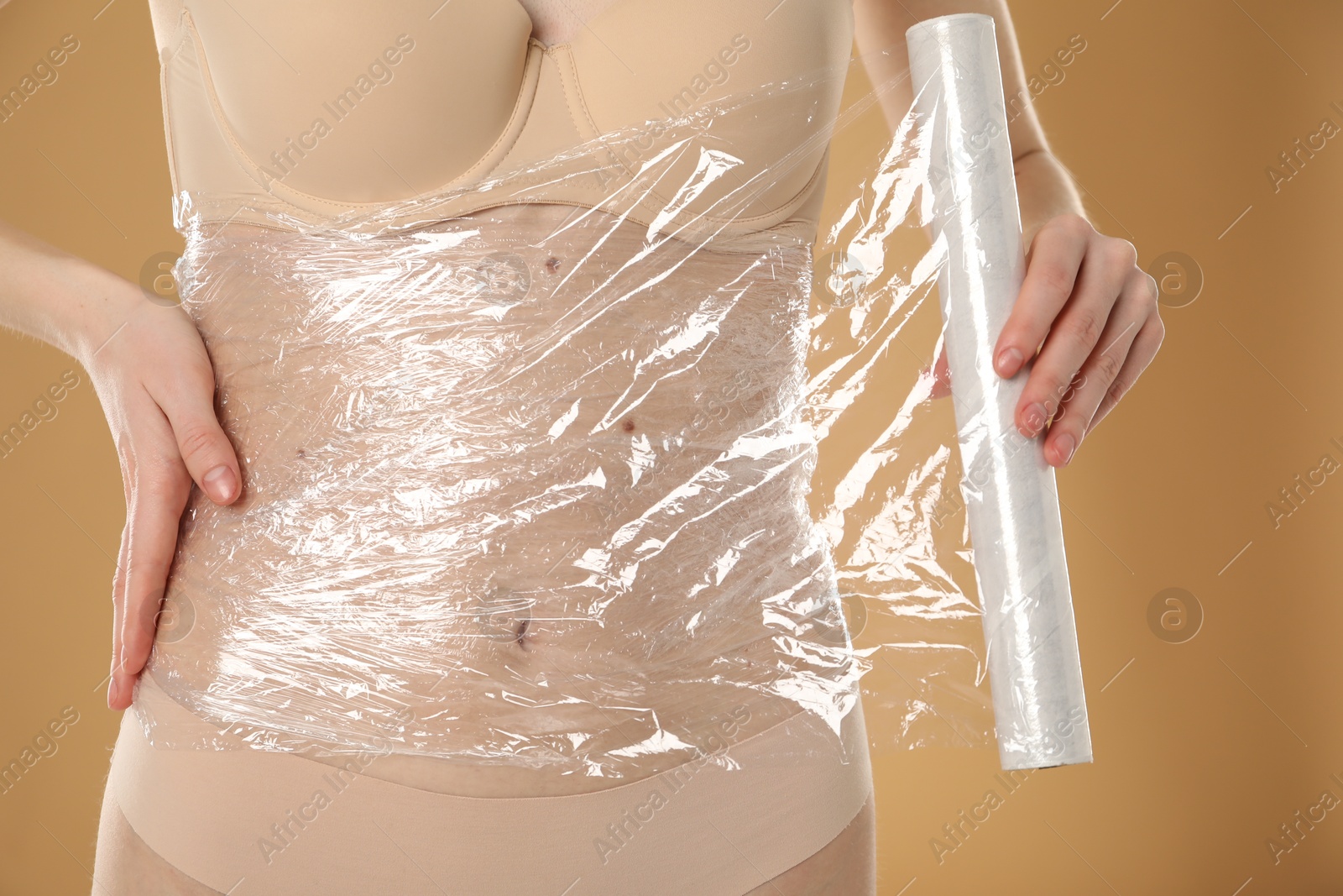 Photo of Woman doing spa body wraps on her belly against beige background, closeup