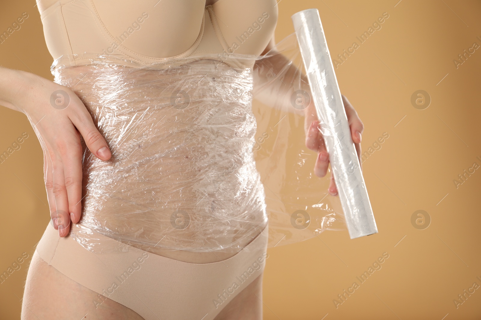 Photo of Woman doing spa body wraps on her belly against beige background, closeup