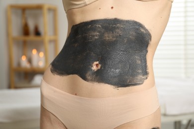 Photo of Woman doing spa body wraps on her belly in salon, closeup