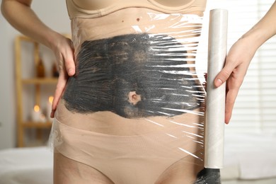 Photo of Woman doing spa body wraps on her belly in salon, closeup