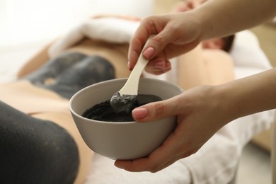 Photo of Esthetician applying cosmetic product for body wraps treatment onto woman's leg in spa salon, closeup