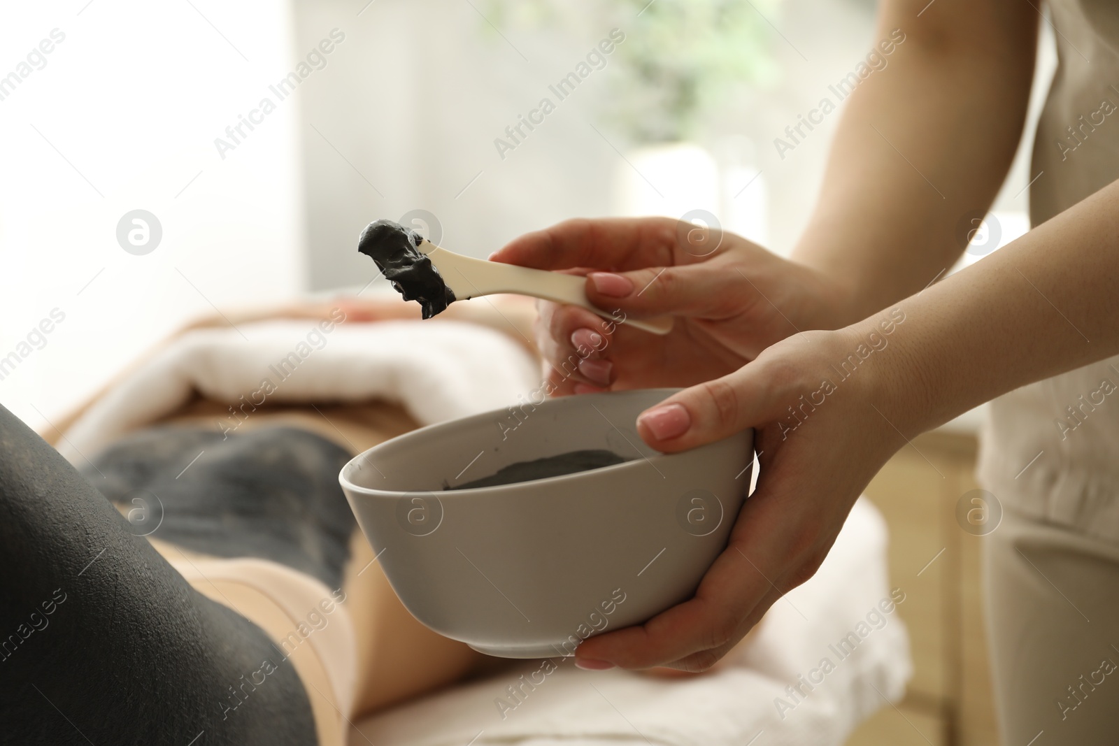 Photo of Esthetician applying cosmetic product for body wraps treatment onto woman's leg in spa salon, closeup