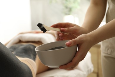 Photo of Esthetician applying cosmetic product for body wraps treatment onto woman's leg in spa salon, closeup