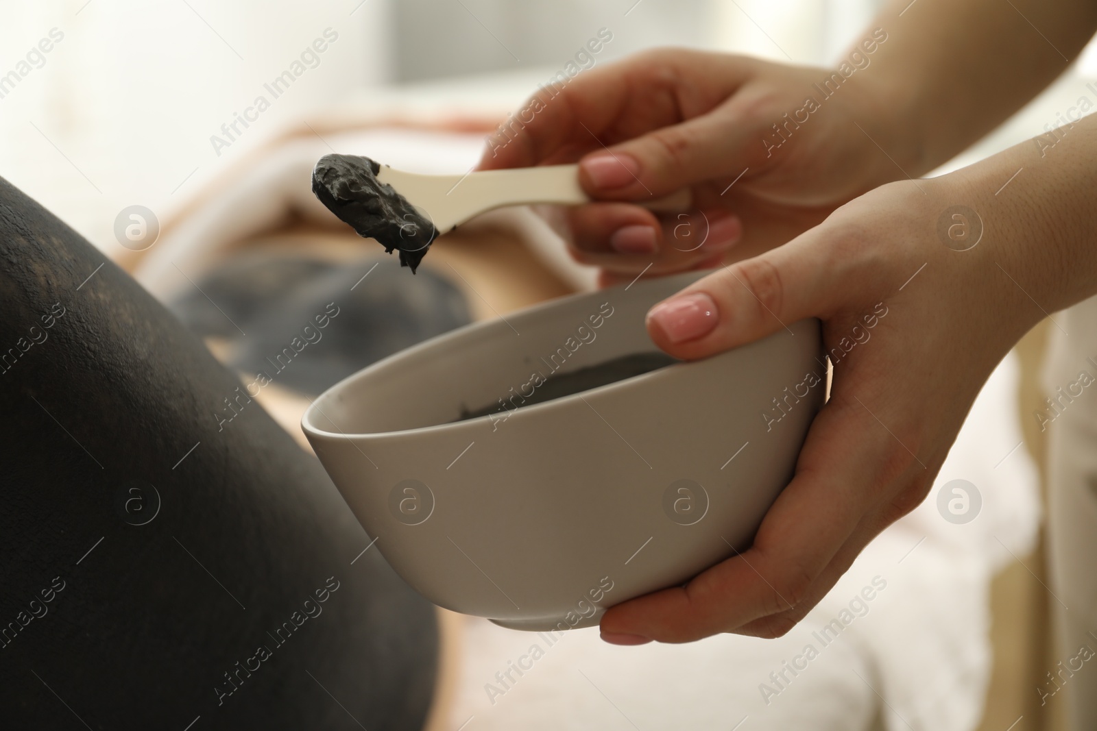 Photo of Esthetician applying cosmetic product for body wraps treatment onto woman's leg in spa salon, closeup