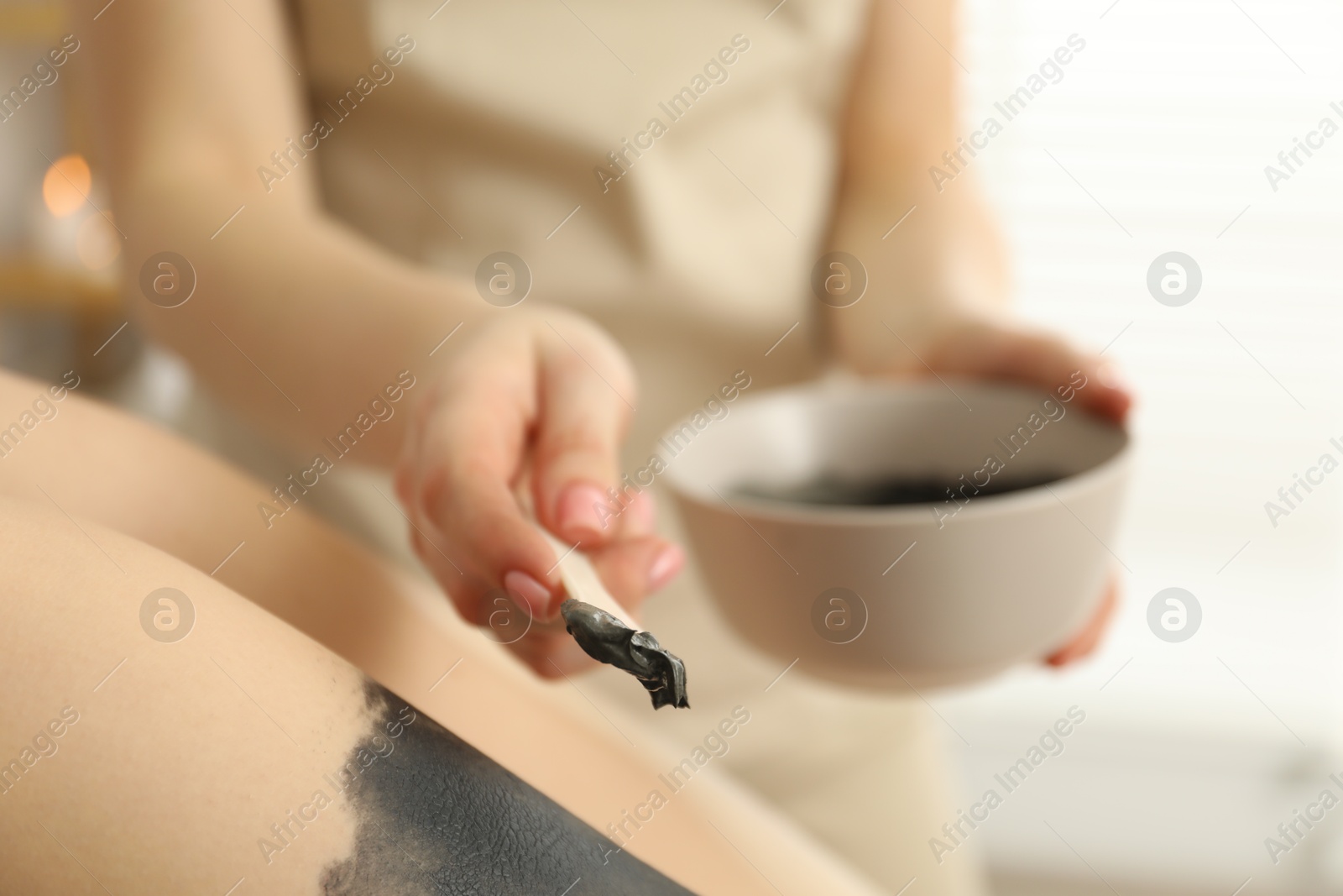 Photo of Esthetician applying cosmetic product for body wraps treatment onto woman's leg in spa salon, closeup