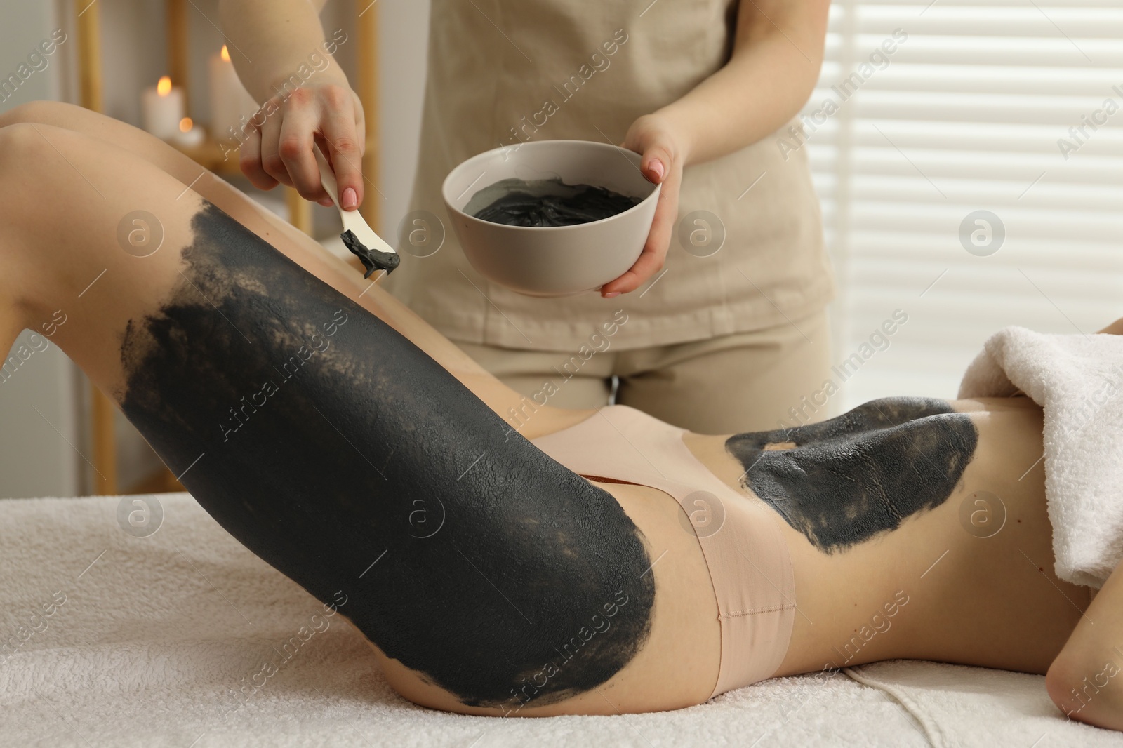 Photo of Esthetician applying cosmetic product for body wraps treatment onto woman's leg in spa salon, closeup