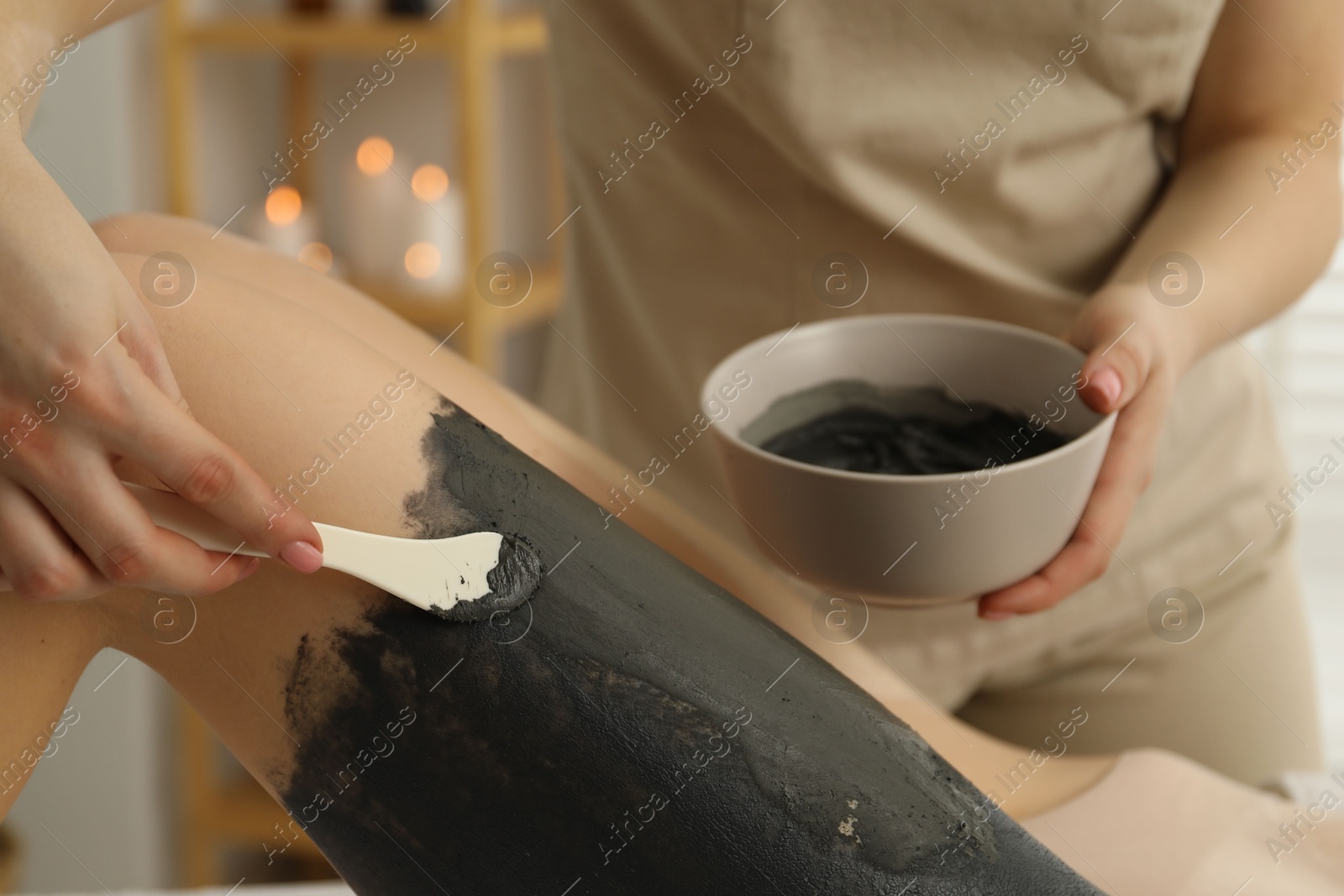 Photo of Esthetician applying cosmetic product for body wraps treatment onto woman's leg in spa salon, closeup