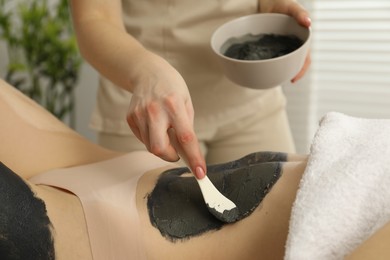 Photo of Esthetician applying cosmetic product for body wraps treatment onto woman's belly in spa salon, closeup