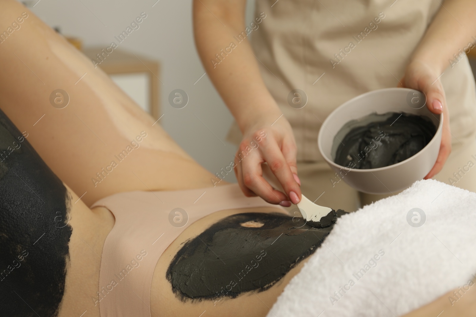 Photo of Esthetician applying cosmetic product for body wraps treatment onto woman's belly in spa salon, closeup